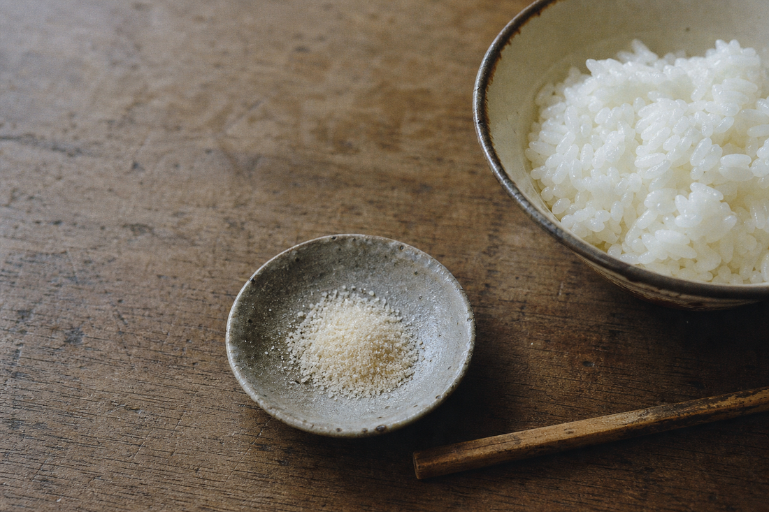 Ceramic dish of umami seasoning beside rice on a worn wooden table